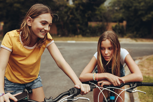 Two cheerful girls riding bicycles outdoors. Girls sitting on bicycles and talking to each other.