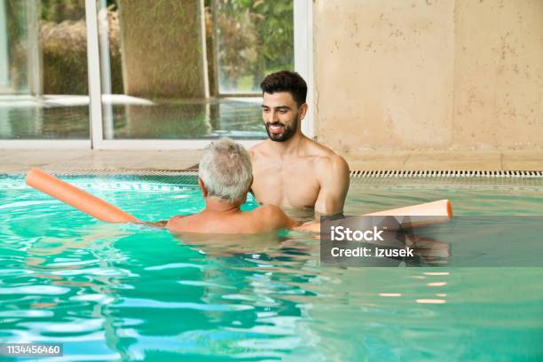 Smiling Instructor Assisting Man With Noodle Float Stock Photo - Download Image Now - Rear View, Senior Men, Noodle Float