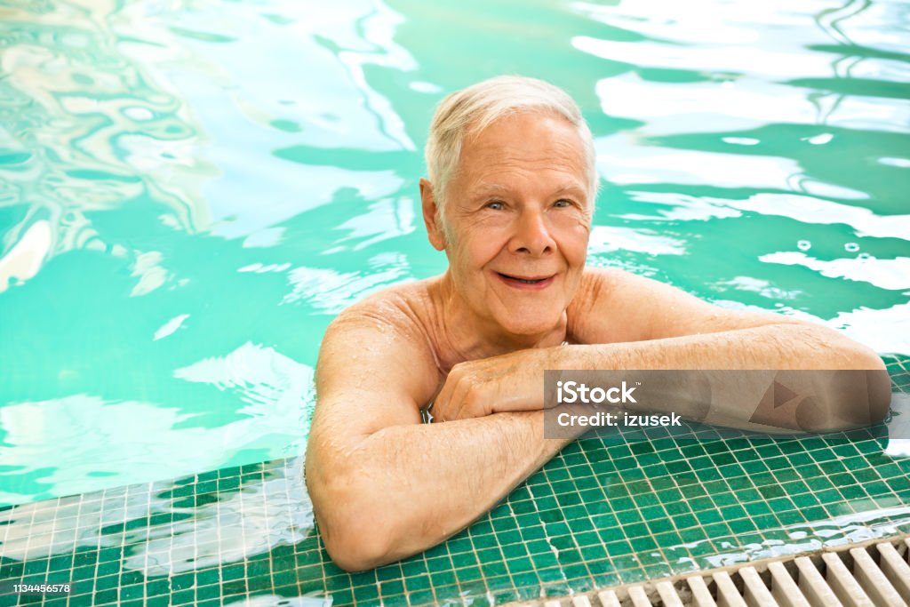 Smiling retired senior man leaning at poolside Portrait of smiling shirtless retired man at nursing home. High angle view of senior male is leaning at poolside. He is in swimming pool. Assisted Living Stock Photo
