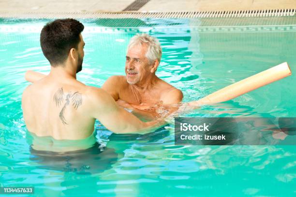 Instructor Assisting Senior Man With Noodle Float Stock Photo - Download Image Now - Water Aerobics, Front View, Looking
