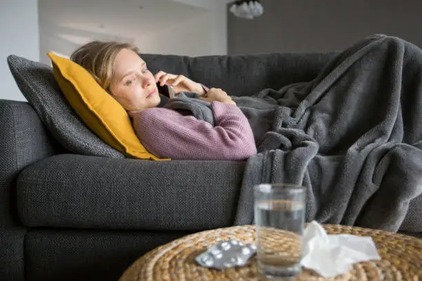 Photo of Sick woman lying on sofa and calling doctor on mobile phone