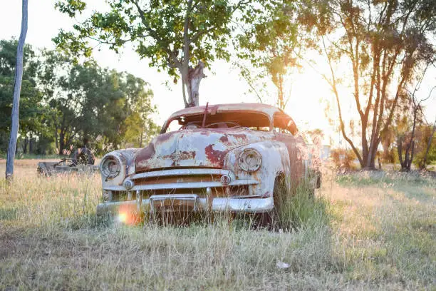 Old rusty abandoned car in bush land at sunset with sun flare