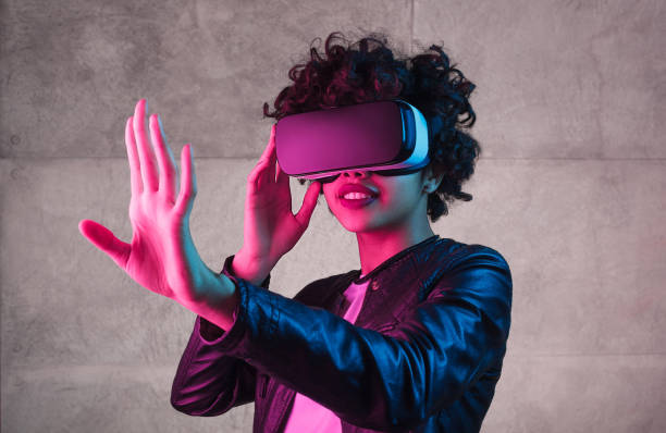 Cute black teenager exploring virtual reality near concrete wall Lovely African American teen girl trying to interact with virtual reality while standing near concrete wall under bright light cyberspace stock pictures, royalty-free photos & images