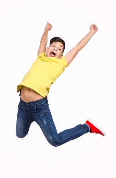 Adorable boy in casual outfit screaming and looking at camera while leaping up in excitement on white background