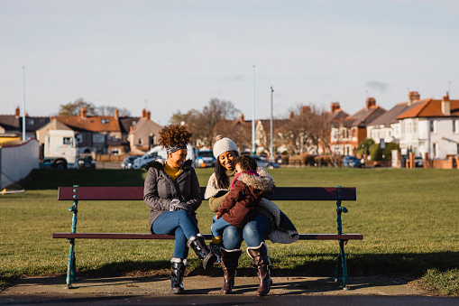 Mother, daughter and grandmother sitting on a bench in a park.