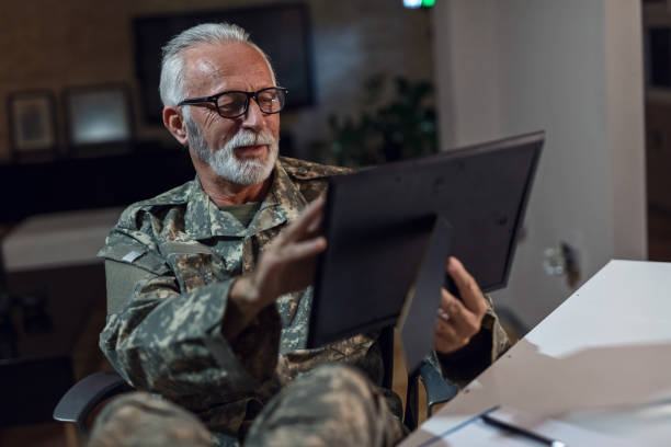 istock Nostalgic senior army soldier looking at photo frame while relaxing in the office. 1134476444