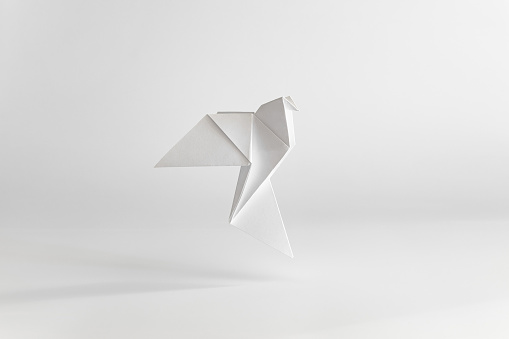 Origami dove made of white paper on white plain background. Minimal concept.
