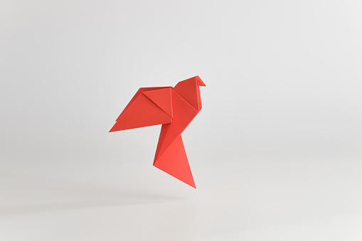 Origami dove made of red paper on white plain background. Minimal concept.