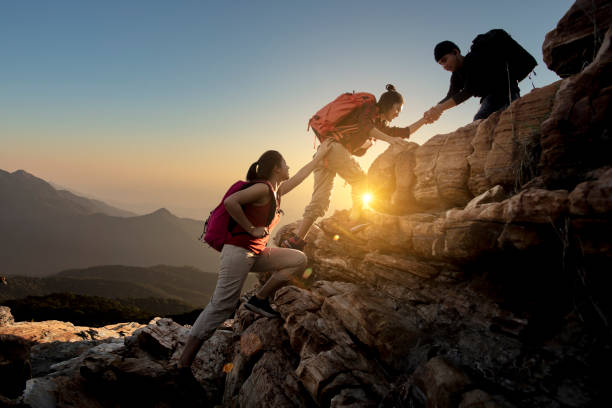 アジアハイキングのグループは、太陽の光と山の中でお互いのシルエットを助けます。 - people traveling journey group of people hiking ストックフォトと画像