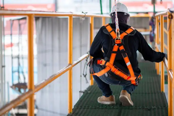 Photo of Construction worker wearing safety harness and safety line working on construction.