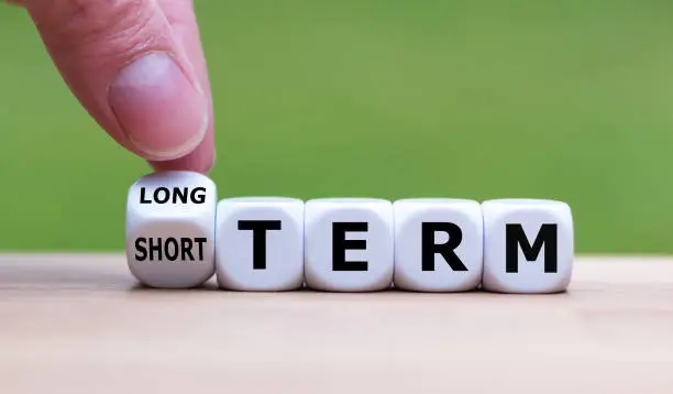 Hand turns a dice and changes the expression "SHORT TERM" to "LONG TERM" (or vice versa).