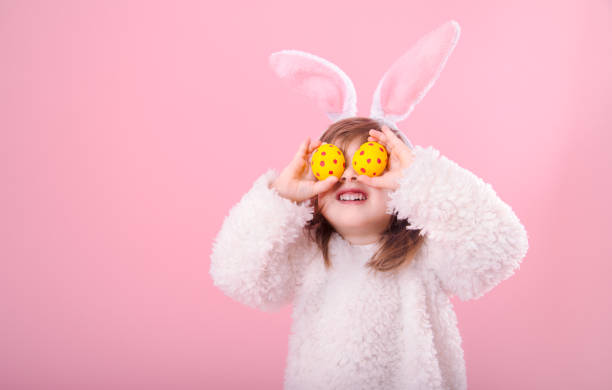 Portrait of a little girl with Bunny ears and Easter eggs Portrait of cute little girl with Bunny ears and yellow Easter eggs in red polka dots, closes eyes with testicles, isolated on pink background easter egg photos stock pictures, royalty-free photos & images
