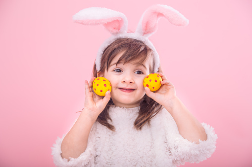 Portrait of a cute little girl with Bunny ears and yellow Easter eggs in red polka dots isolated on pink background