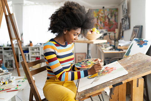 Beautiful fine art painter drawing in studio, holding color palette. Wears casual colorful clothes