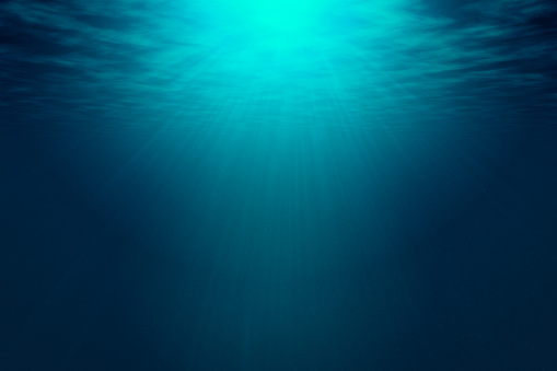 Deep blue sea with rays of sunlight, ocean surface seen from underwater. Background texture with copy space for text or product display.