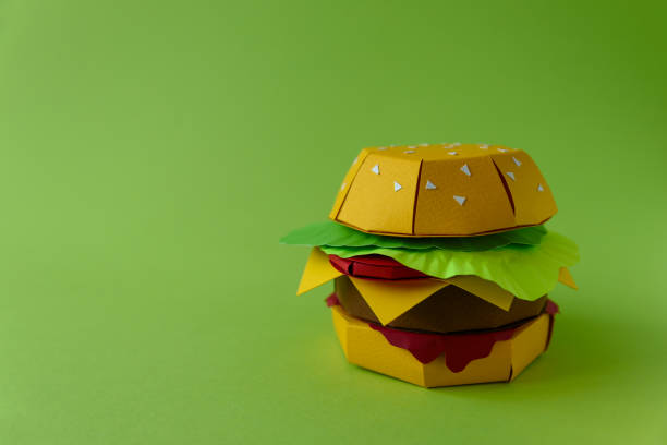 istock Paper cheeseburger with beef, cheese, tomato, lettuce and sauce on a green background. Copy space. Creative or art food concept 1134487651