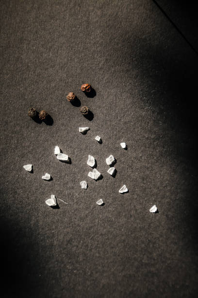 Spices, top view of spilled salt and pepper grains on dark background, studio shot.