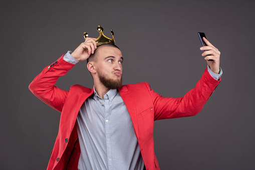 Joven barbudo hombre guapo en corona de oro tomando selfie mirando en el teléfono inteligente photo