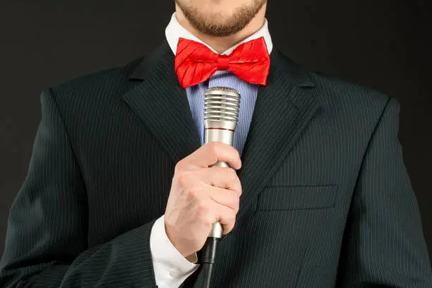 closeup portrait of unshaved man holding microphone in his hand. red bow-tie. showman, black suit