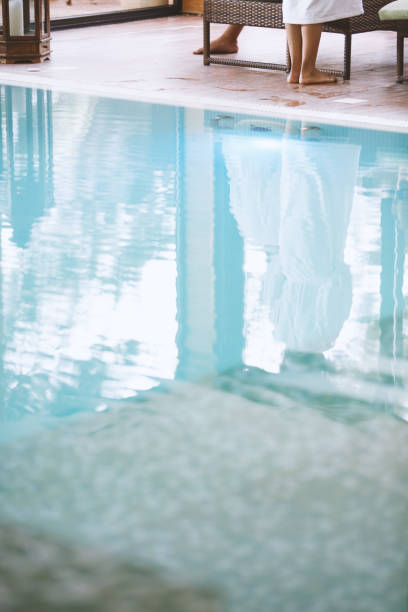 Crystal clear water of the swimming pool with reflection of women standing on poolside.