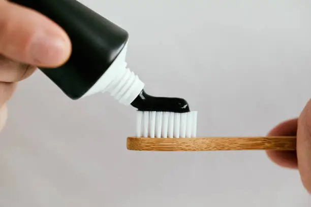 Photo of Male hands with a black toothpaste and a bamboo toothbrush