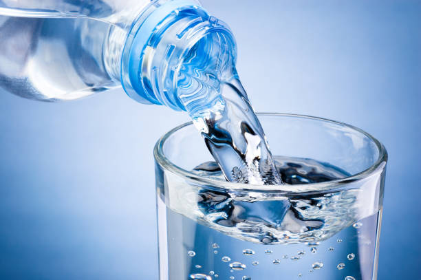 istock Pouring water from bottle into glass on blue background 1134529345