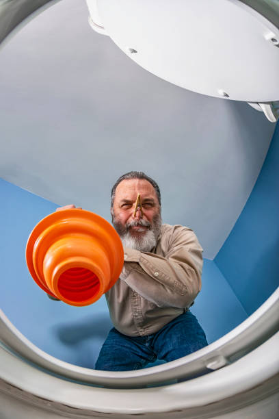 Looking up at a man using orange plunger to clear a clogged toilet