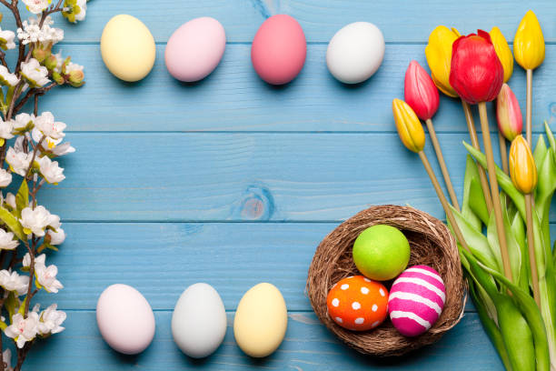 istock Colorful easter eggs in easter nest with flowers on blue wooden background 1134545628