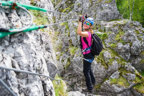 Photo of Happy young girl crossing a via ferrata wire bridge in Baia de Fier, Romania. Indian bridge on a klettersteig with a joyful, adventurous woman stepping across it.