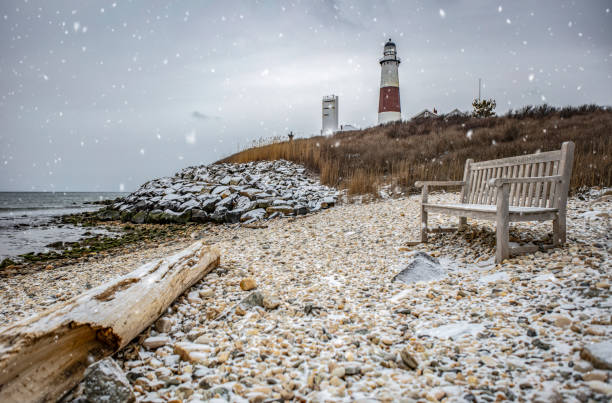 Snowy Day at Montauk Lighthouse Photograph of Montauk Lighthouse, shore, and bench in foreground with snow coming down montauk point stock pictures, royalty-free photos & images