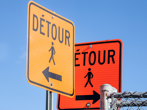 Picture of two construction signs, in orange color, taken in Montreal, Quebec, Canada, indicating a detour compulsory for pedestrians
