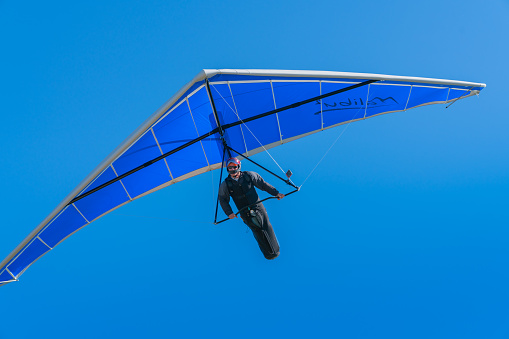 Hang glider pilot flying towards under bright blue wing and sky in February 2019 Mount Maunganui New Zealand