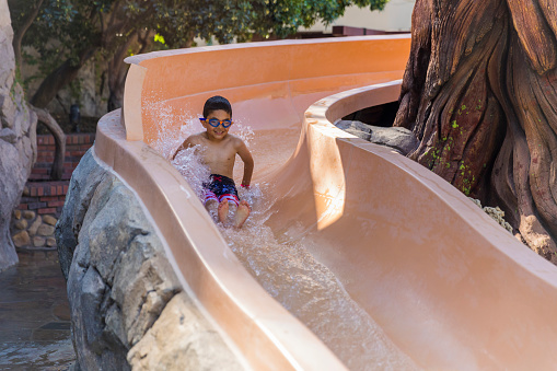 High quality stock photo of a  7-year-old child sliding into a clear and clean swimming pool on a water slide.