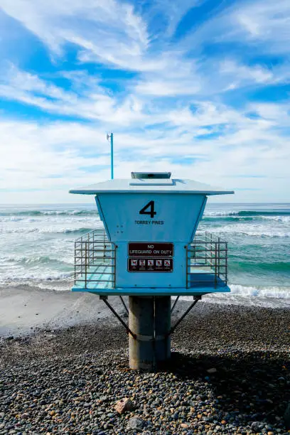 Photo of Blue lifeguard tower on a rocky sand beach with clouded blue sky sunny end of day.