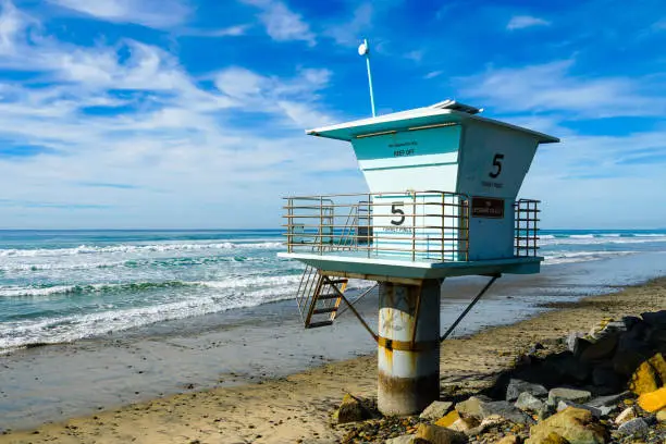 Photo of Blue lifeguard tower on a rocky sand beach with clouded blue sky sunny end of day.