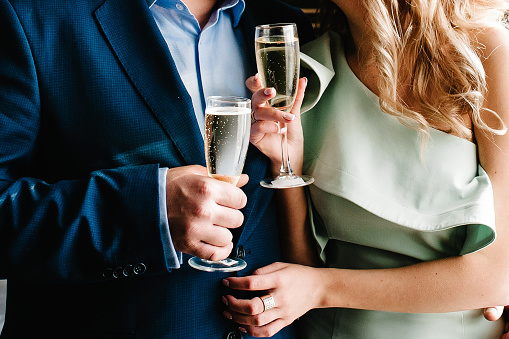 The bride and groom holds a glass of champagne and stand in the room. Close up. Holiday. Look at the glasses.