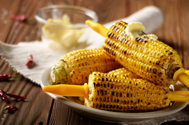 istock Wooden table with deep grilled sweet corn cobs under melting butter with plastic holder on clay dish 1134610699