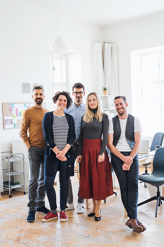 A full length portrait of group of young businesspeople standing in a modern office, looking at camera.