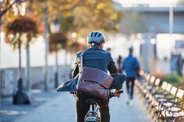Photo of A rear view of businessman commuter with electric bicycle traveling to work in city.