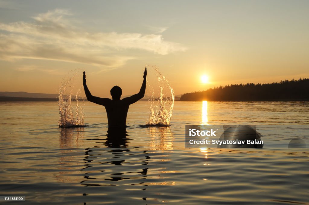 Sagoma di un uomo sullo sfondo del tramonto. Il ragazzo in vita si tuffò nel mare. Spruzza acqua a mano. - Foto stock royalty-free di Acqua