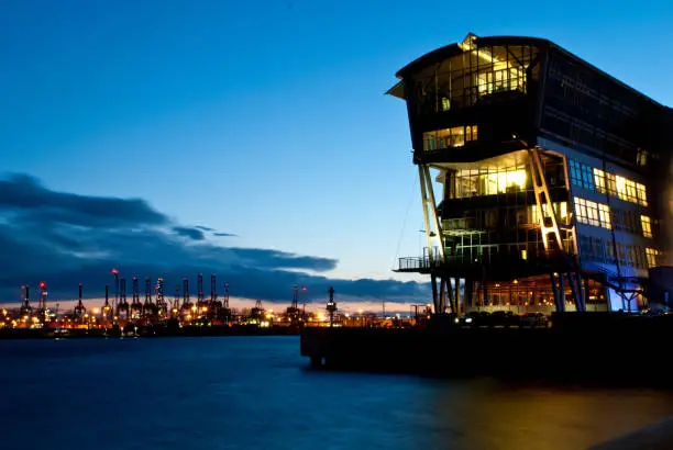 Office building at night, at the fishing port, Port of Hamburg, Altona, Elbe river. I n the background the cranes of Hamburg harbor