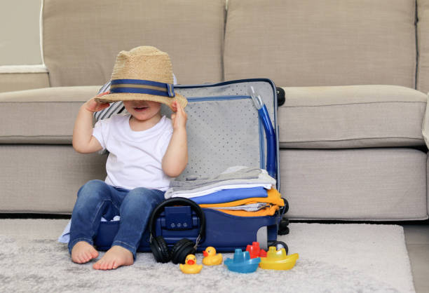 cute funny little baby boy siiting in blue suitcase with hat on his eyes, packed for vacation full of clothes ready for traveling. vacation with child. - packing duck imagens e fotografias de stock
