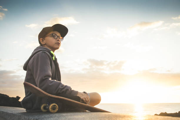 istock Boy Sitting On Retaining Wall By Beach Against Sky During Sunset 1134646312