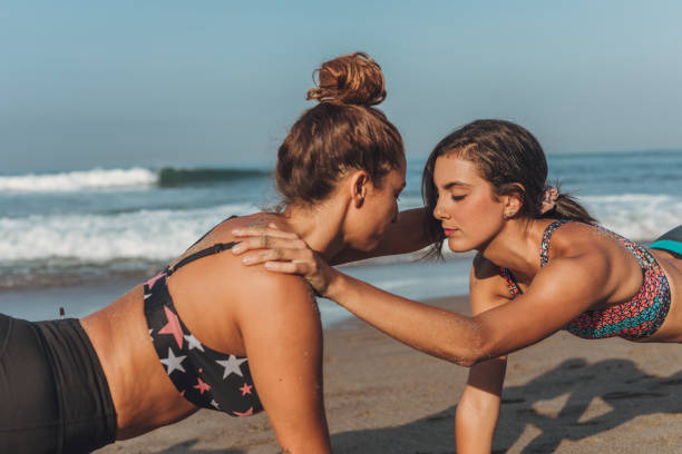 Two young women doing yoga meditation and stretching exercises at beach