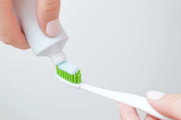 istock Woman hand holding new white toothbrush with green bristles and putting paste from toothpaste tube. Gray background. People teeth hygiene concept. Closeup. 1134677603