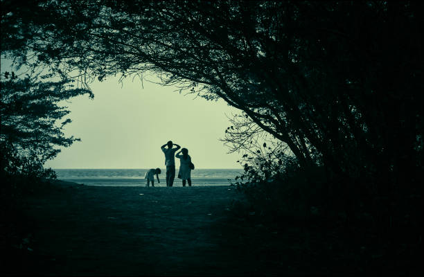 Silhouette of a family looking through the horizon, across the naturally formed tree arches at Henry Island of Bay of Bengal, a popular but secluded sea beach in West Bengal.\nPictured here a child accompanied by her parents entering the beach. \nPhoto taken on 05/01/2014 at Bakkhali, West Bengal, India.