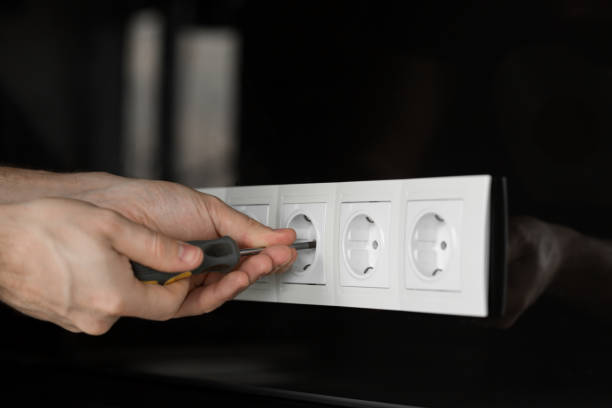 istock Close-up of an electrician's hand with a screwdriver disassembling a white electrical outlet on a black glass wall 1134692796
