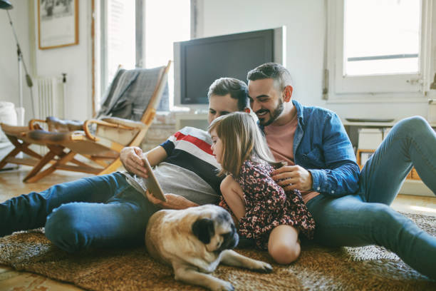 Gay men with daughter using digital tablet at home Gay men with daughter using digital tablet in living room. Family with pug spending weekend together. They are at home. gay daddy stock pictures, royalty-free photos & images