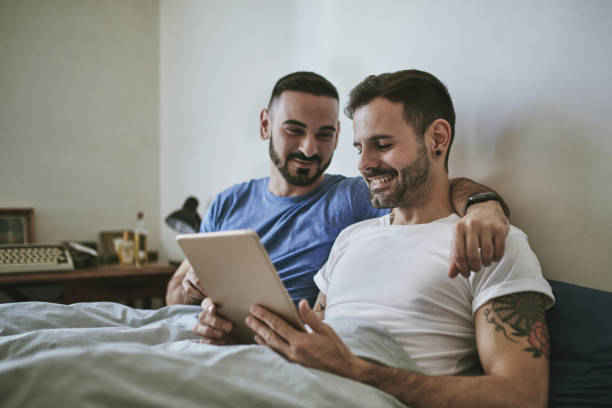 istock Smiling gay couple looking at tablet PC on bed 1134694519