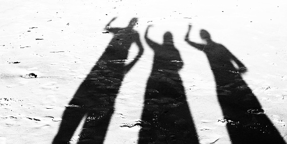 Three people arms raised on the sandy beach.